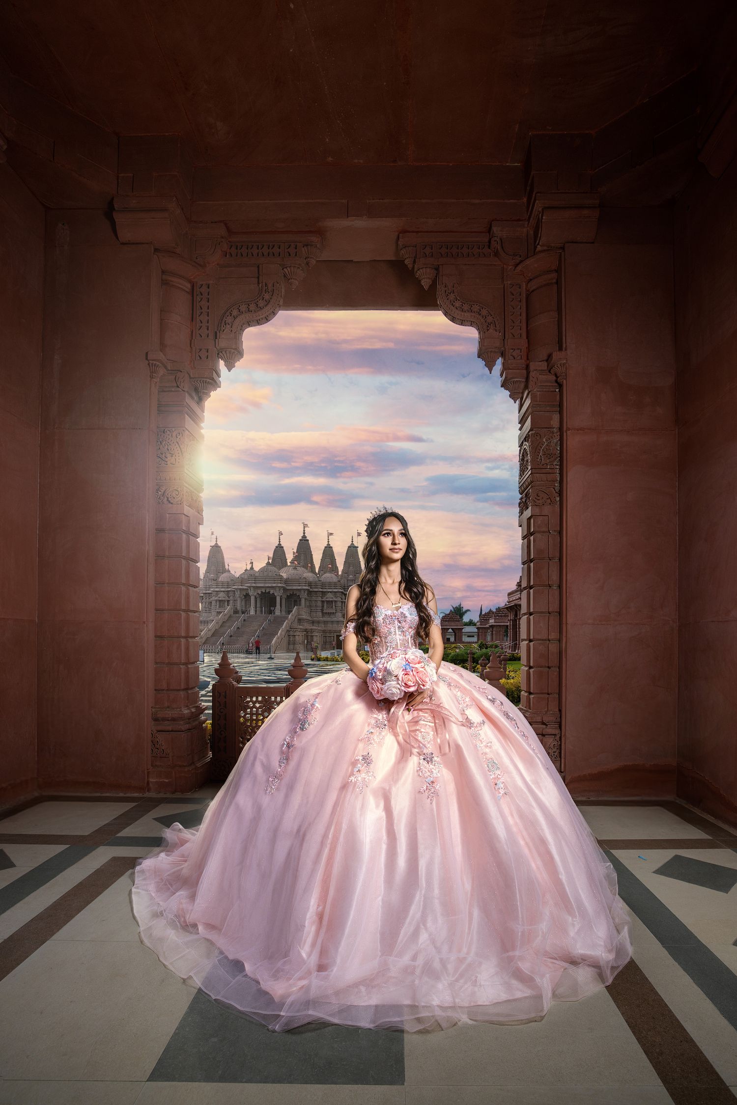 A person in a pink ball gown poses in an archway overlooking a castle during golden hour sunset.