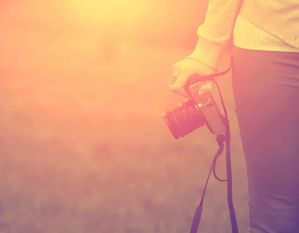 Photographe tenant un appareil photo reflex numérique à l'heure d'or avec la lumière chaude du coucher du soleil en arrière-plan.
