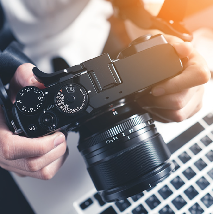 Personne tenant un appareil photo professionnel sans miroir au-dessus d'un ordinateur portable, ajustant les paramètres pour le travail de p