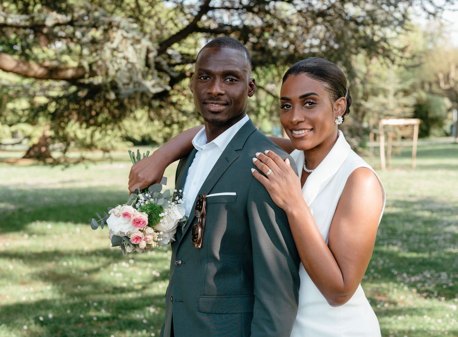 Happy Black couple in wedding attire posing together outdoors with bridal bouquet.