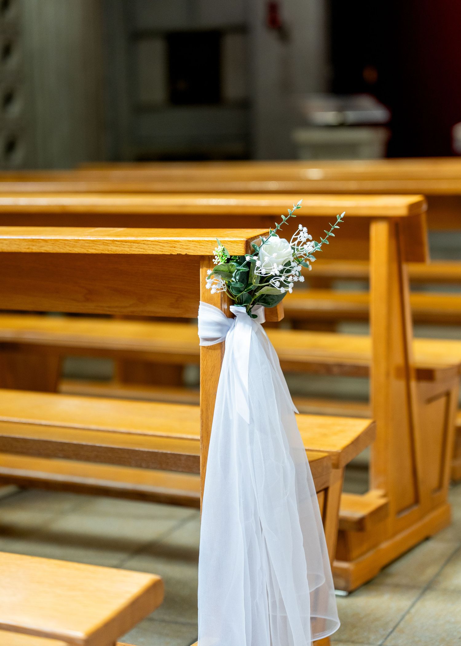 White tulle bow and floral bouquet decorating a wooden church pew for a wedding ceremony.