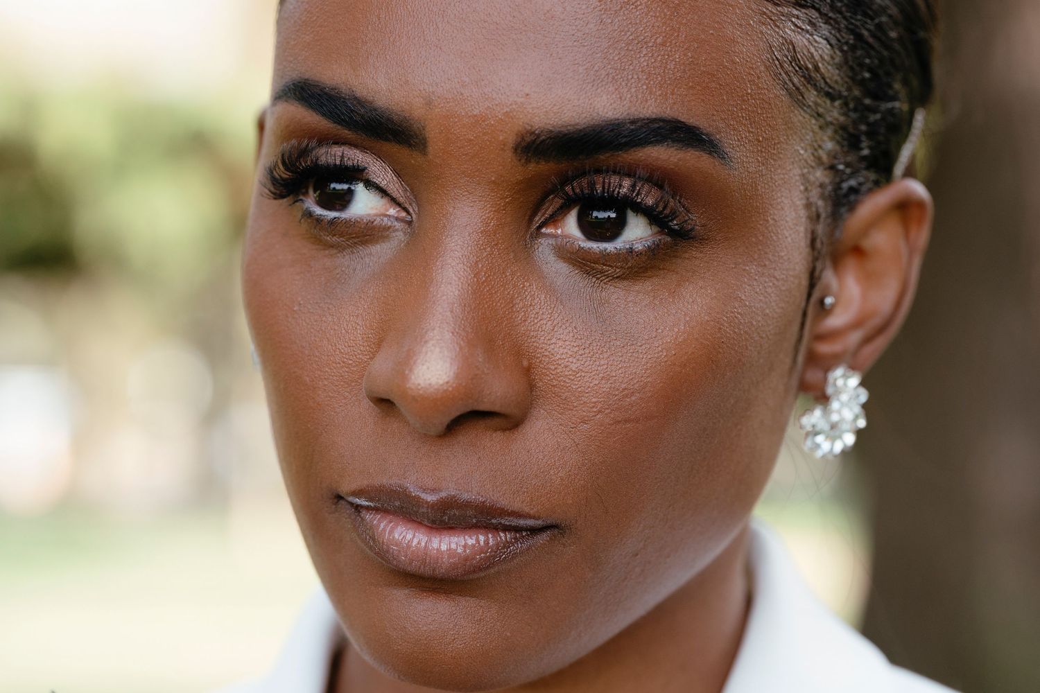 Close-up portrait of a beautiful Black bride wearing crystal earrings with a blurred green background.