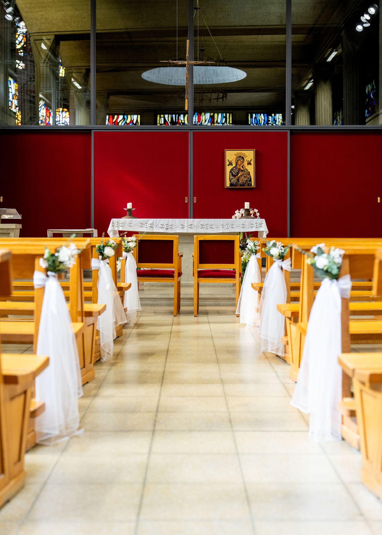 Church aisle decorated with white tulle and floral arrangements on wooden pews, leading to an altar with a religious icon.