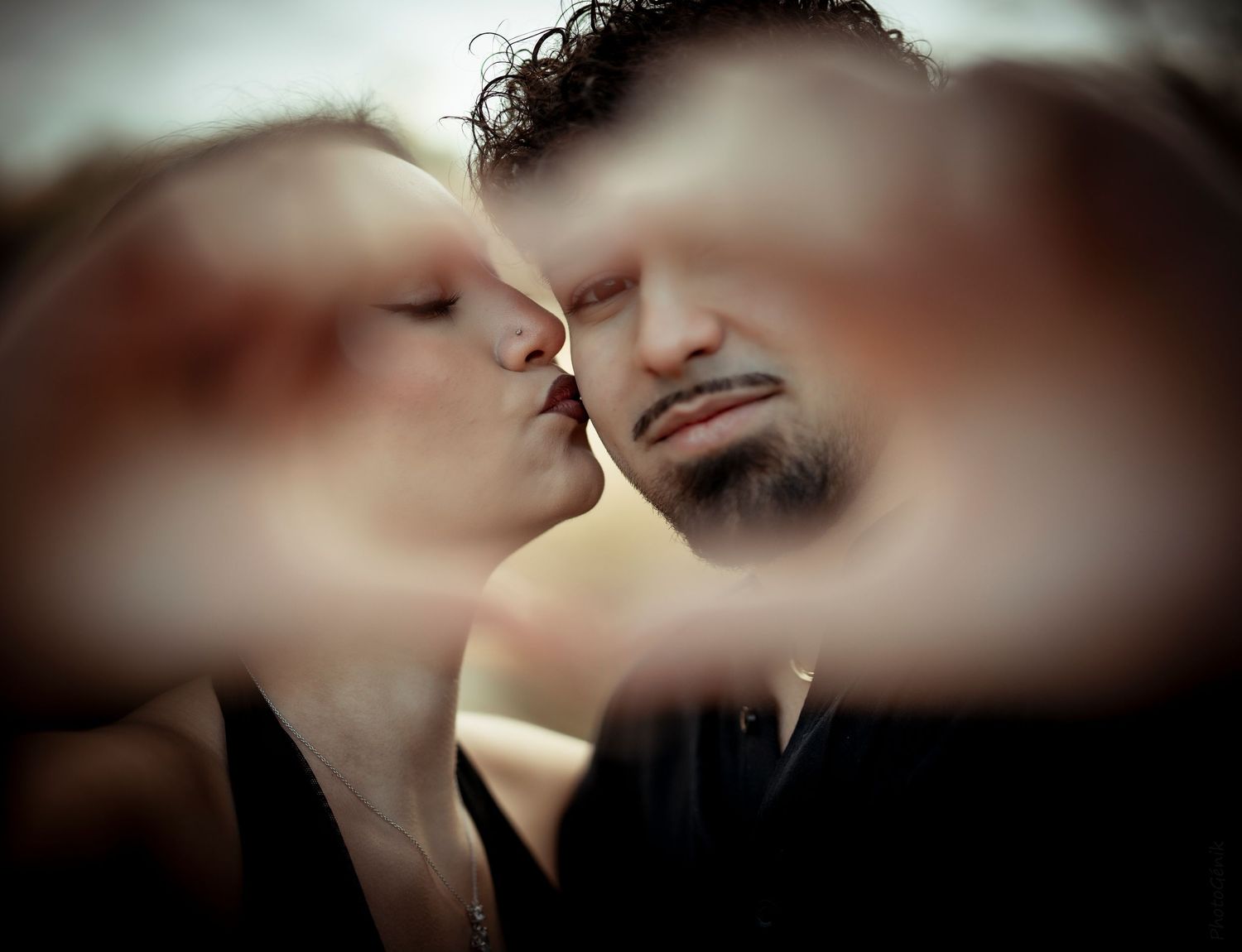 Romantic couple sharing a kiss framed by their hands forming a heart shape in a creative portrait.
