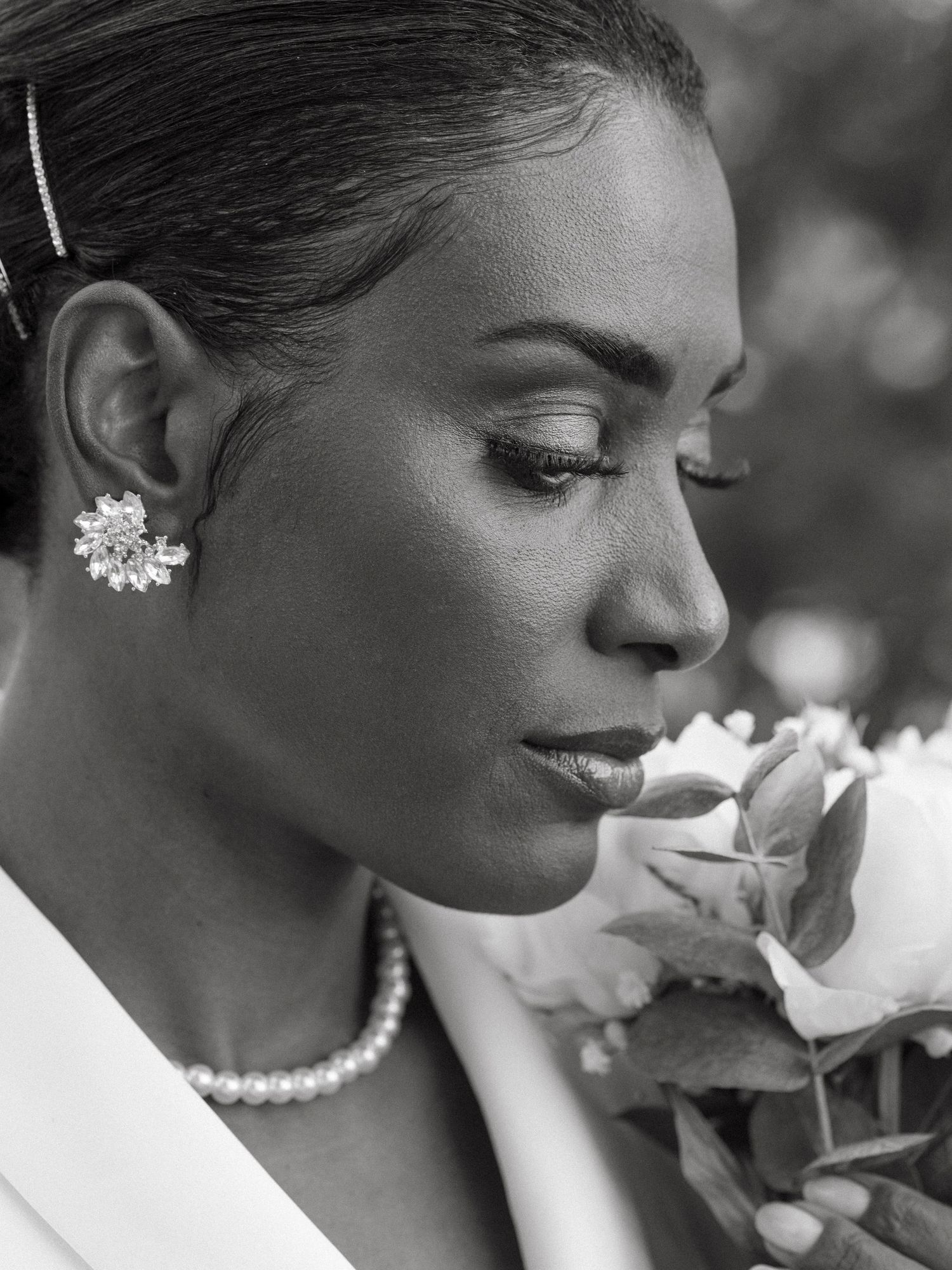 Black and white portrait of a bride smelling a rose, wearing pearl necklace and crystal earrings.