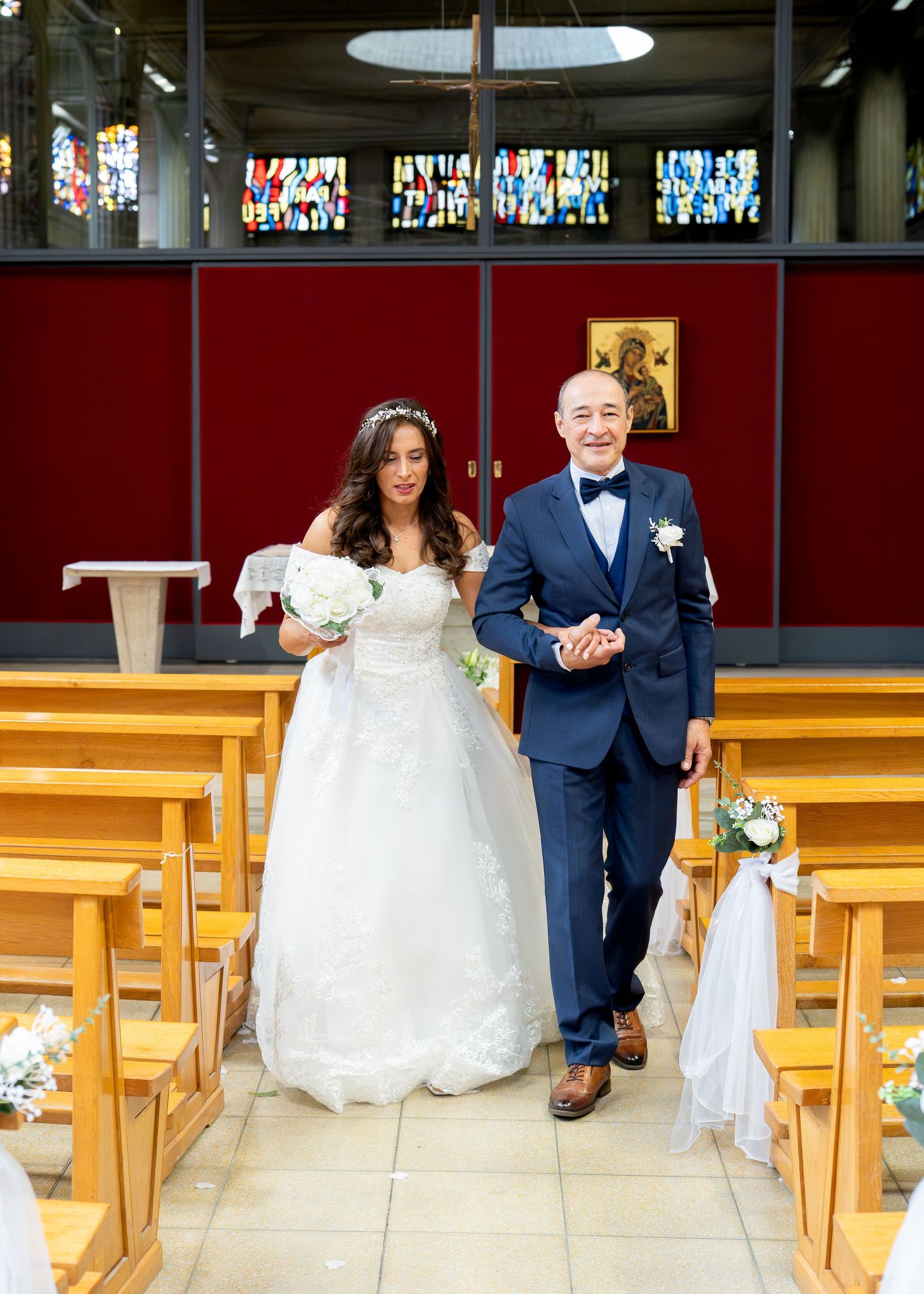 Bride in white gown and groom in navy suit walking down church aisle during wedding ceremony.