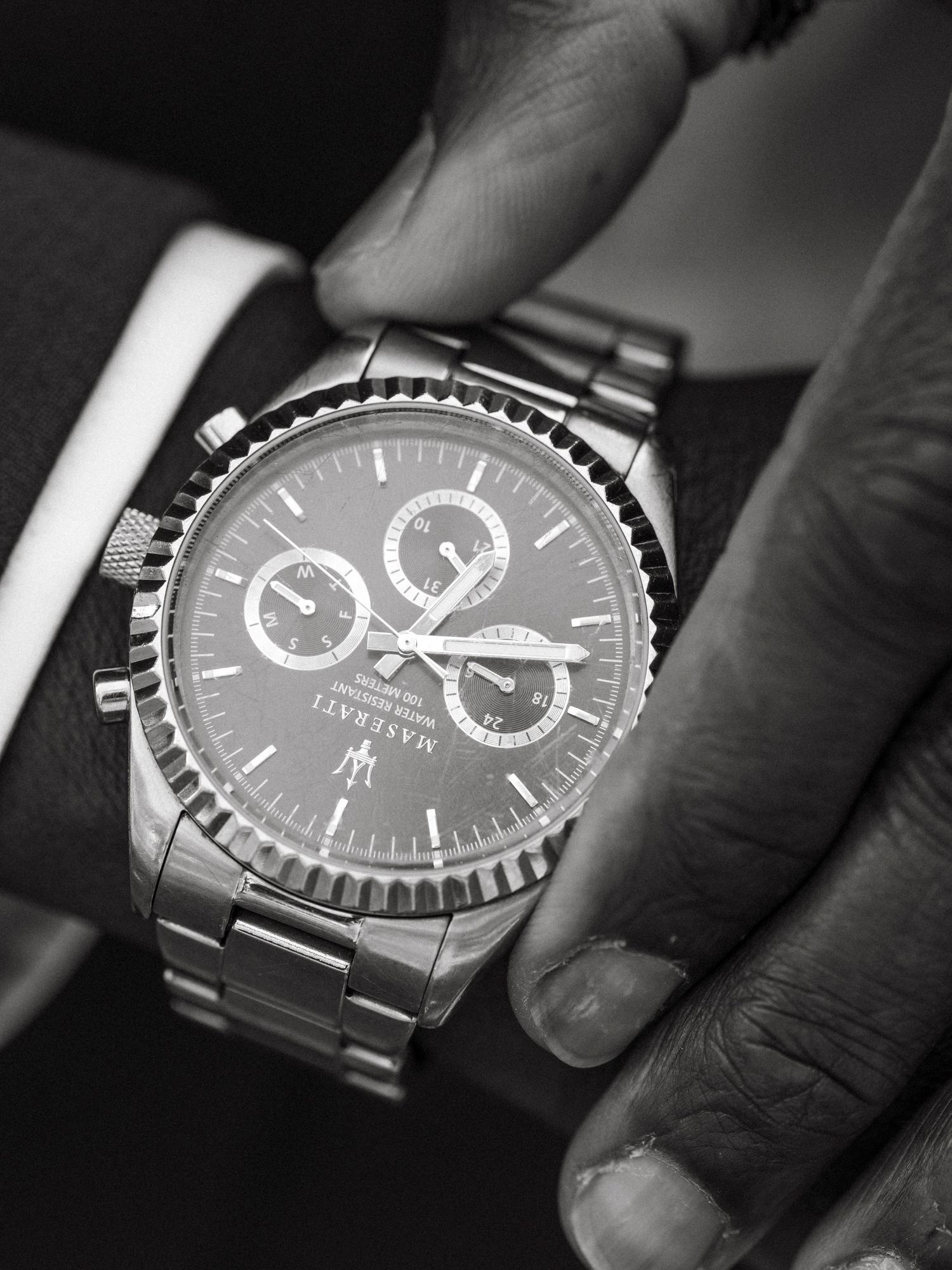 Black and white close-up of groom adjusting a Maserati chronograph watch on his wrist.