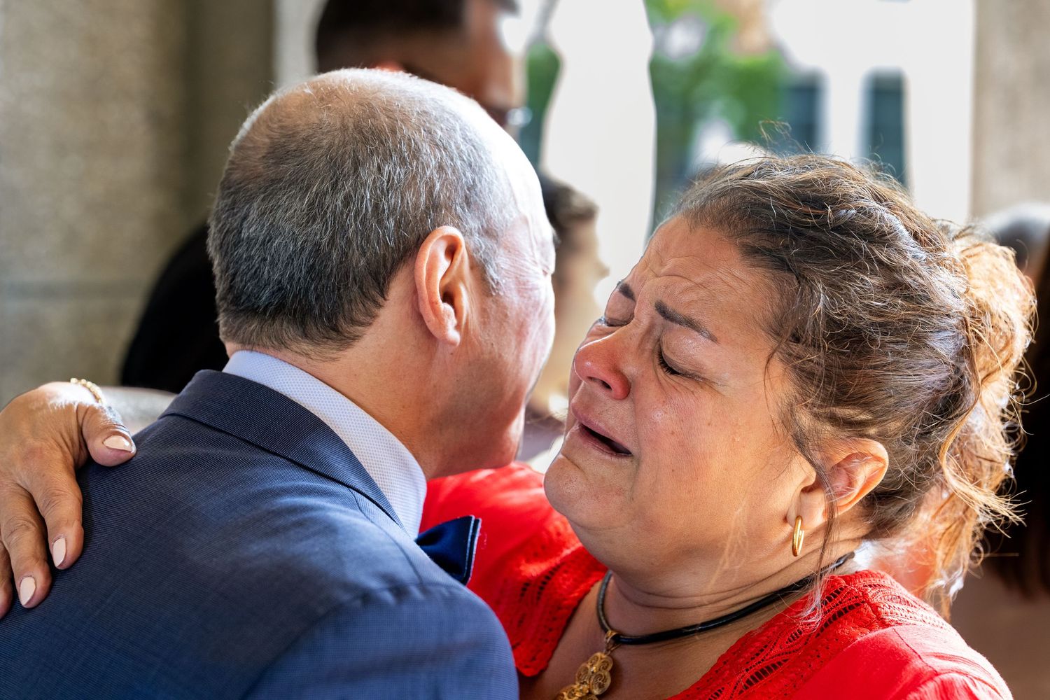 A woman in red cries while embracing a man in a suit during an emotional outdoor encounter.
