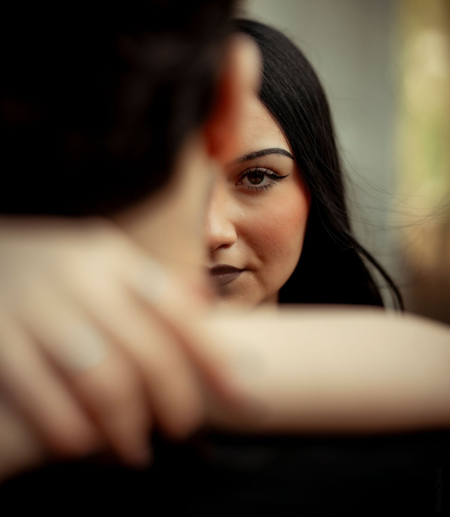 A woman with dark hair gazes intently at someone in the foreground in a shallow depth of field portrait.