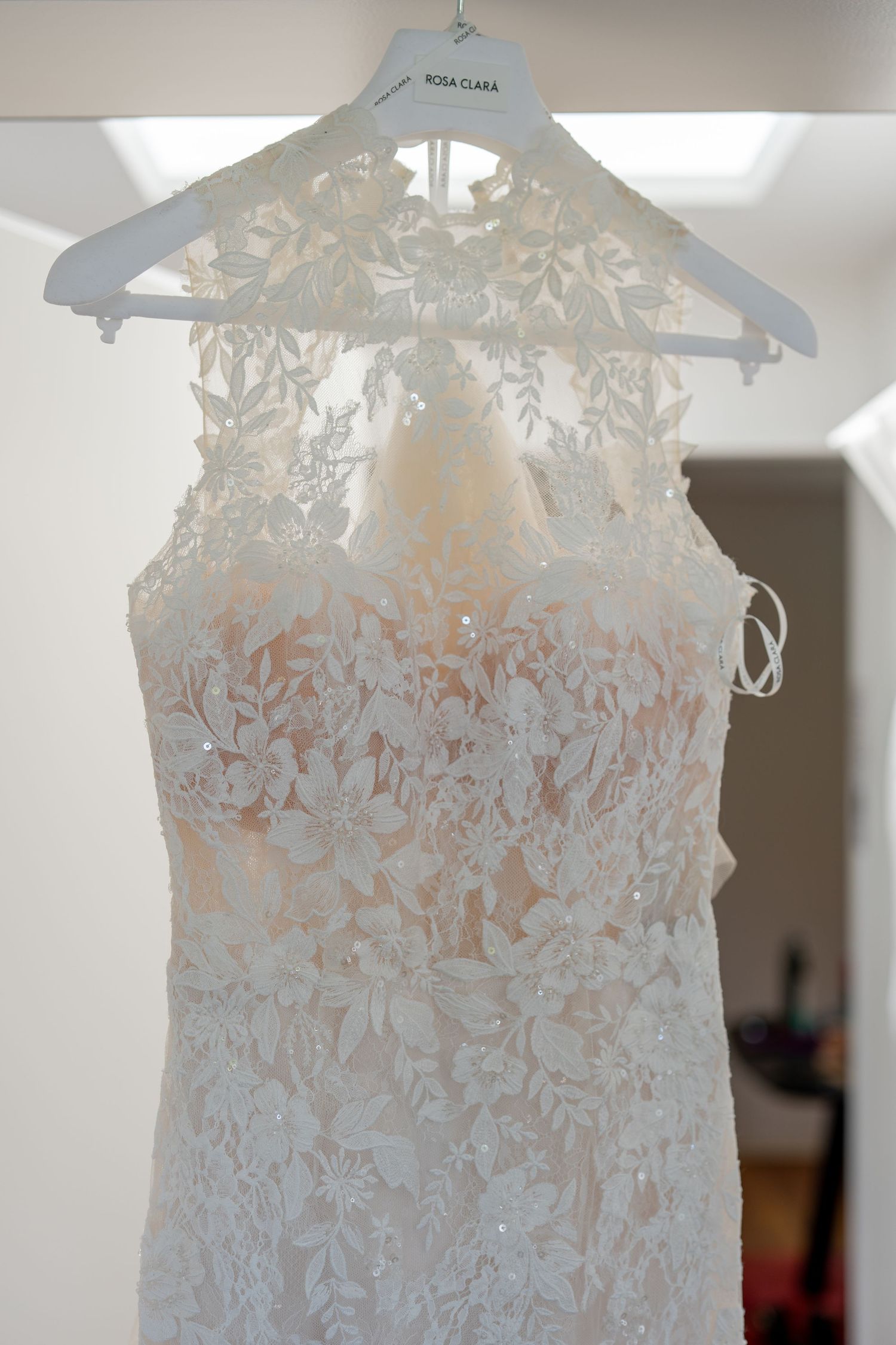 Rosa Clara white lace bridal gown with floral appliques hanging on a designer hanger in a bright room.