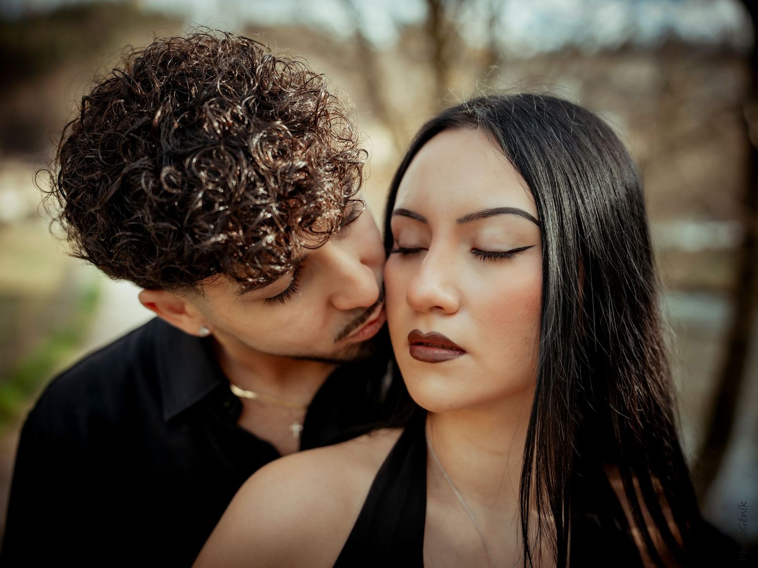 Romantic couple portrait with curly-haired man gently kissing woman with long dark hair on the cheek.