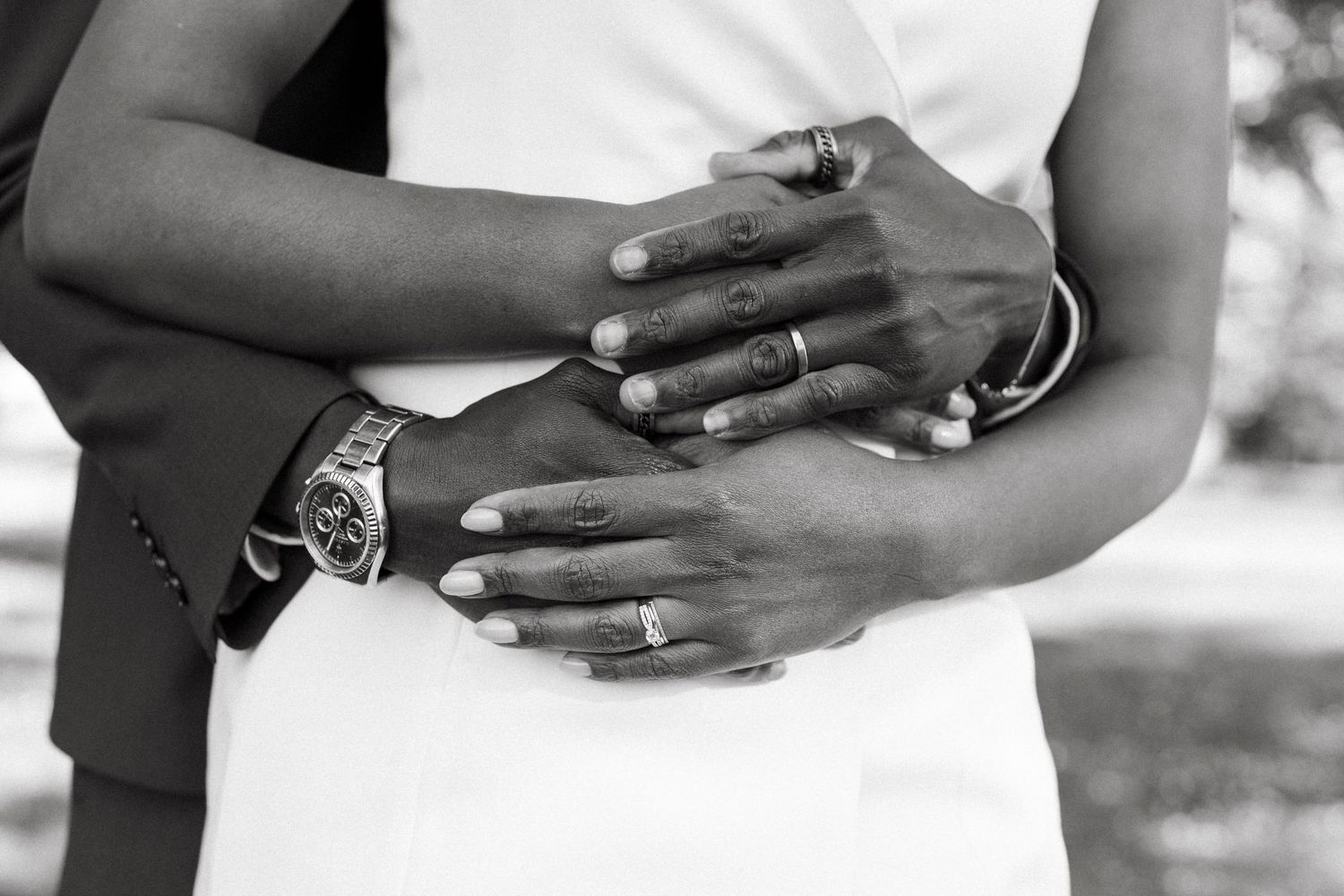 Black and white close-up of a couple's intertwined hands showing wedding rings and a silver watch.