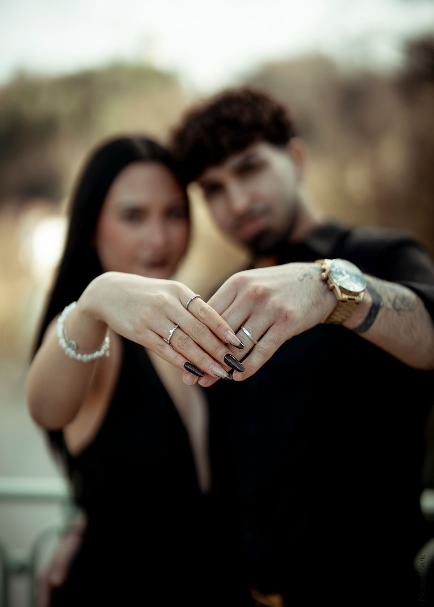 Couple in black outfits displaying matching rings on their hands in a focused engagement photo.