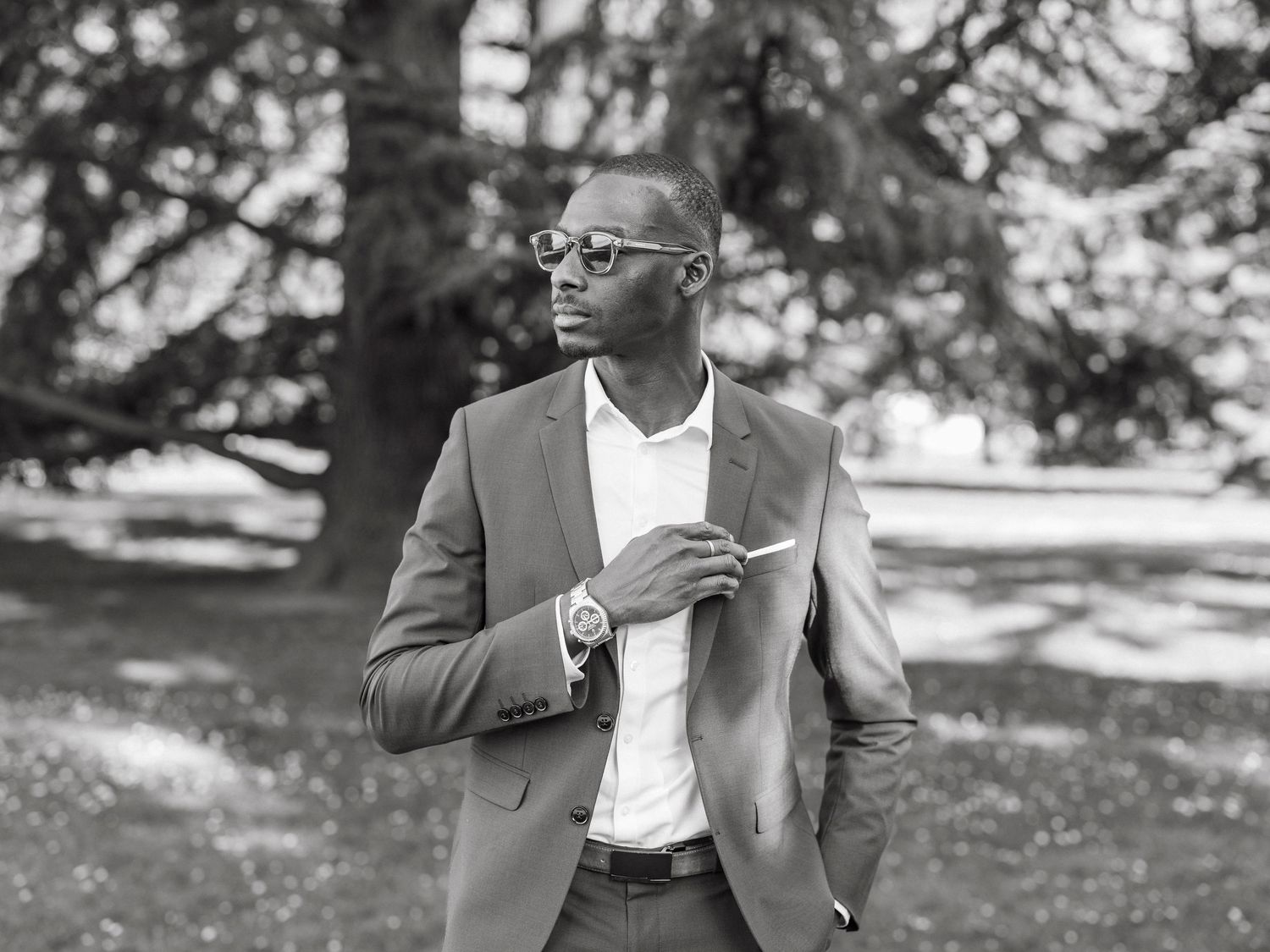 Dapper Black man in suit and sunglasses posing outdoors in black and white photo.