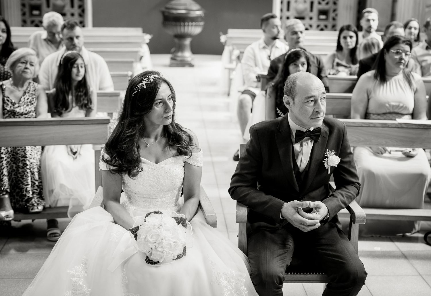 Black and white photo of bride and groom sitting at church altar during wedding ceremony.