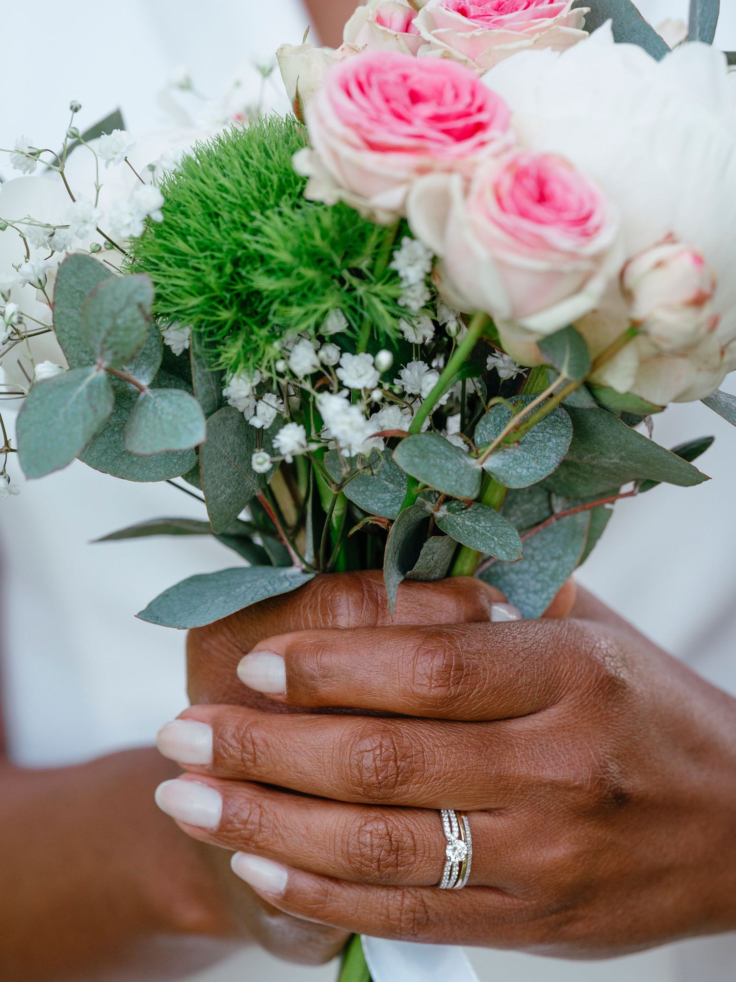 Close-up of bride holding colorful wedding bouquet with pink roses and green flowers, wearing a diamond ring.