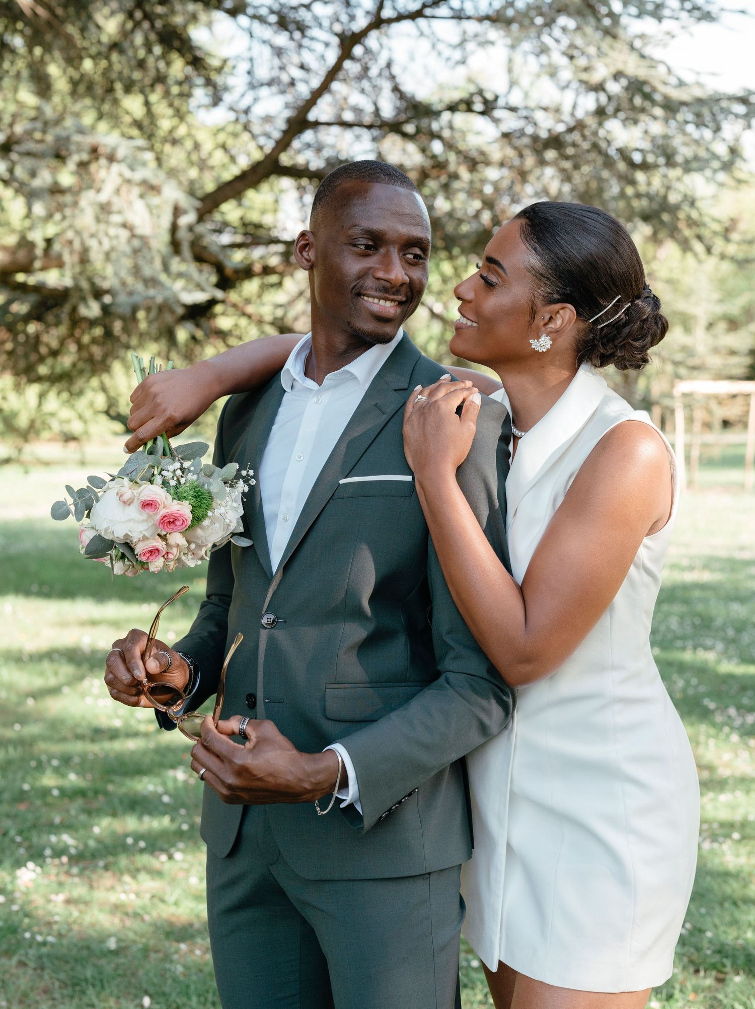 Joyful Black couple sharing a laugh outdoors, groom holding a pink bridal bouquet.