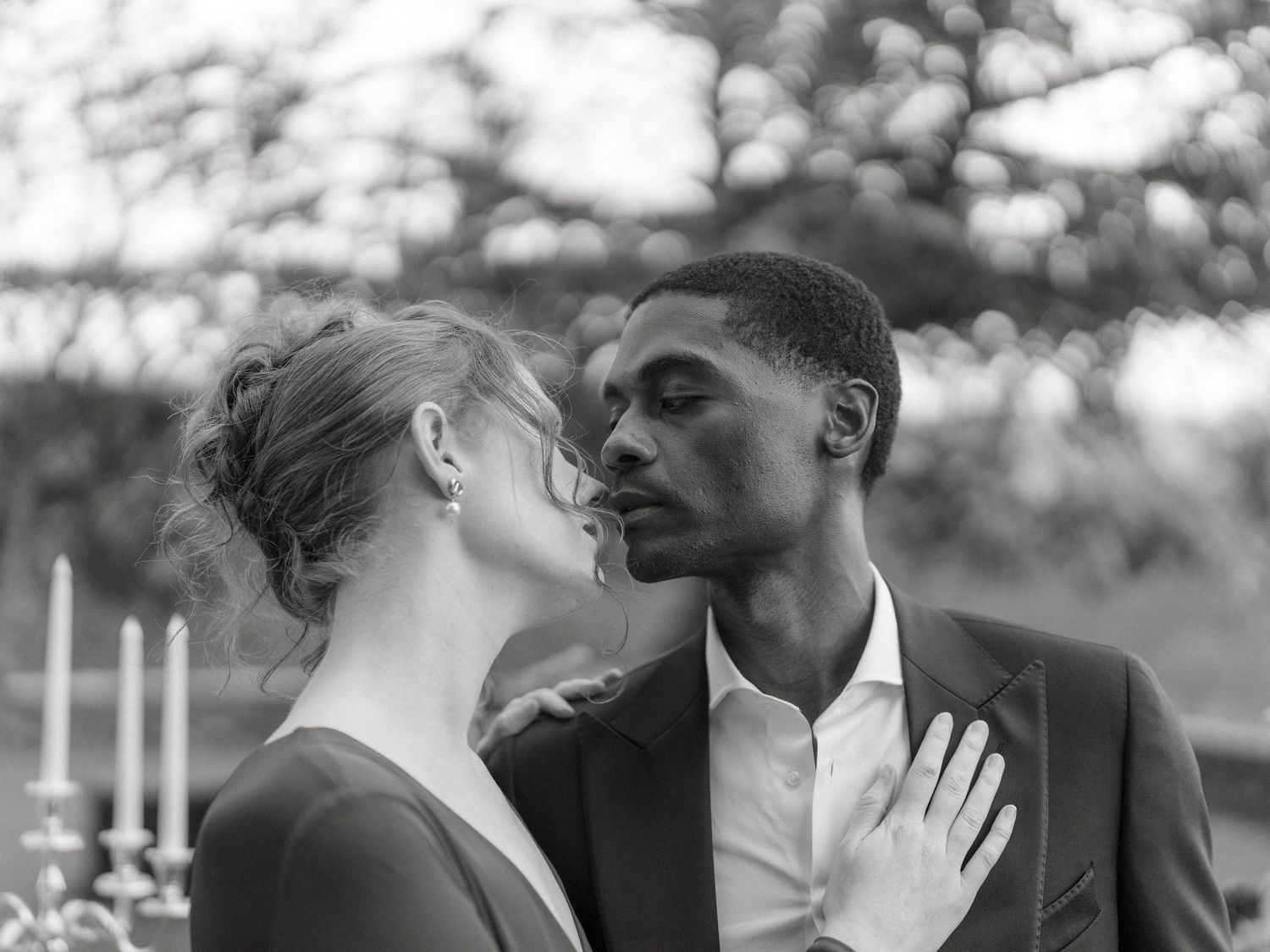 Black and white romantic wedding portrait of interracial couple almost kissing with candelabra.