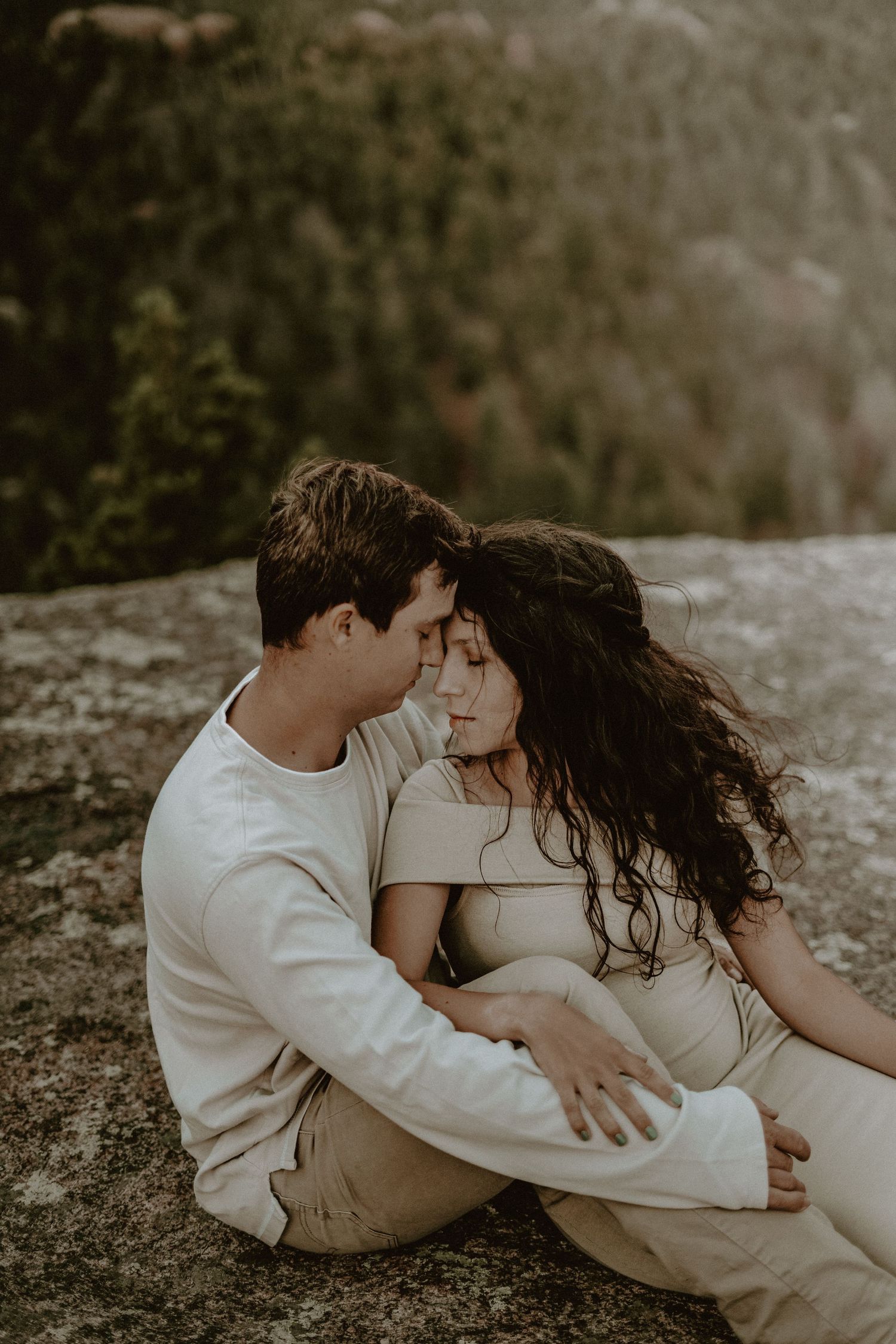 Romantic couple in matching cream attire share intimate moments against a moody outdoor backdrop in Manitou Springs.