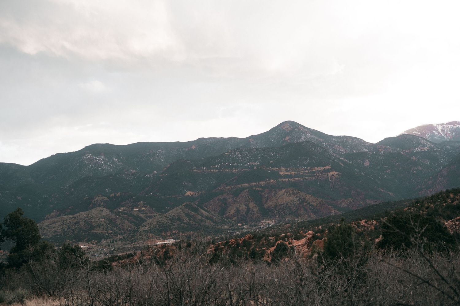 Rugged mountain landscape with rocky peaks and forested slopes under an overcast sky.