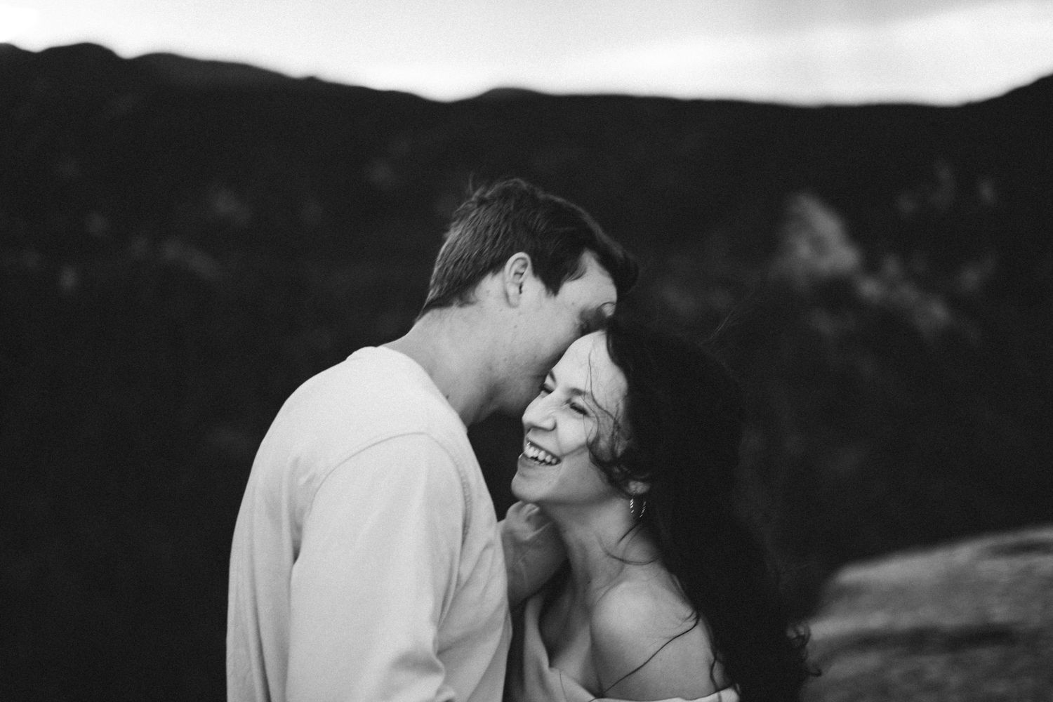 A romantic couple shares an intimate moment against a moody forest backdrop and mountain in Manitou Springs.