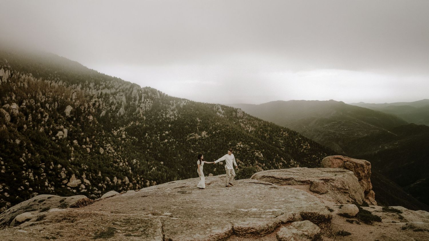 Panoramic mountain landscape in Manitou Springs with couple venturing on distant misty rocky overlook.