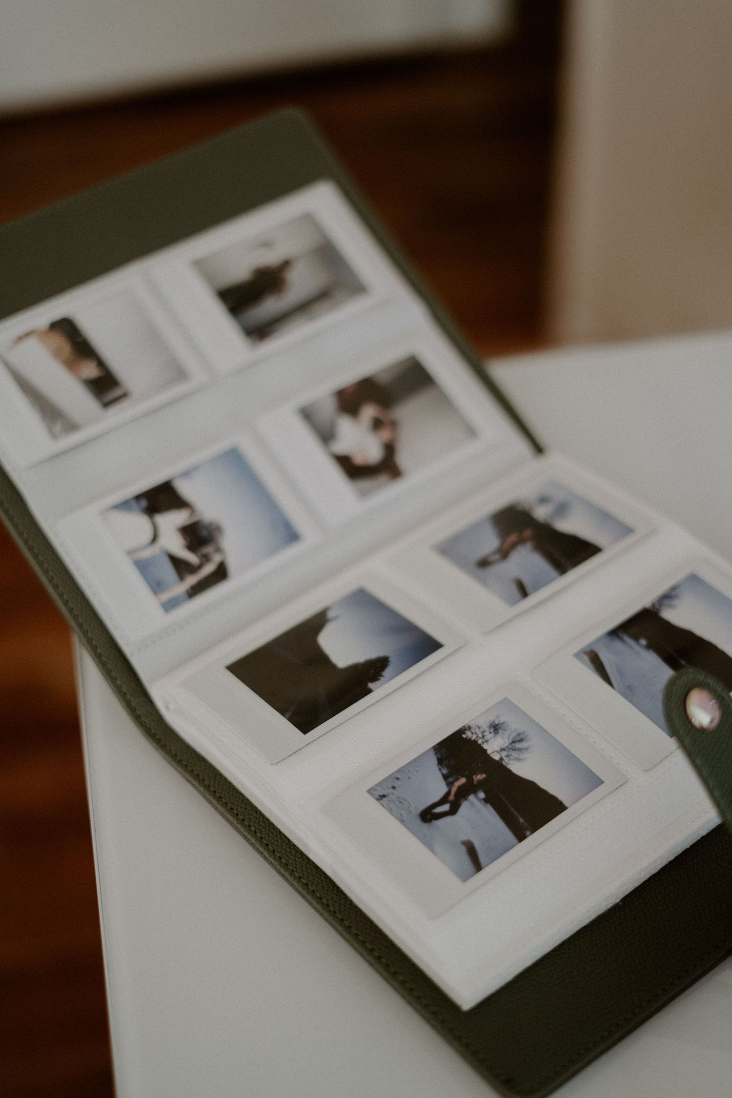Polaroid photo prints arranged in an olive green modern album on a desk.