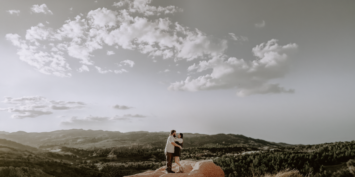 Couple embraces on Garden of the Gods red rocks under cloudy skies in mountain landscape.