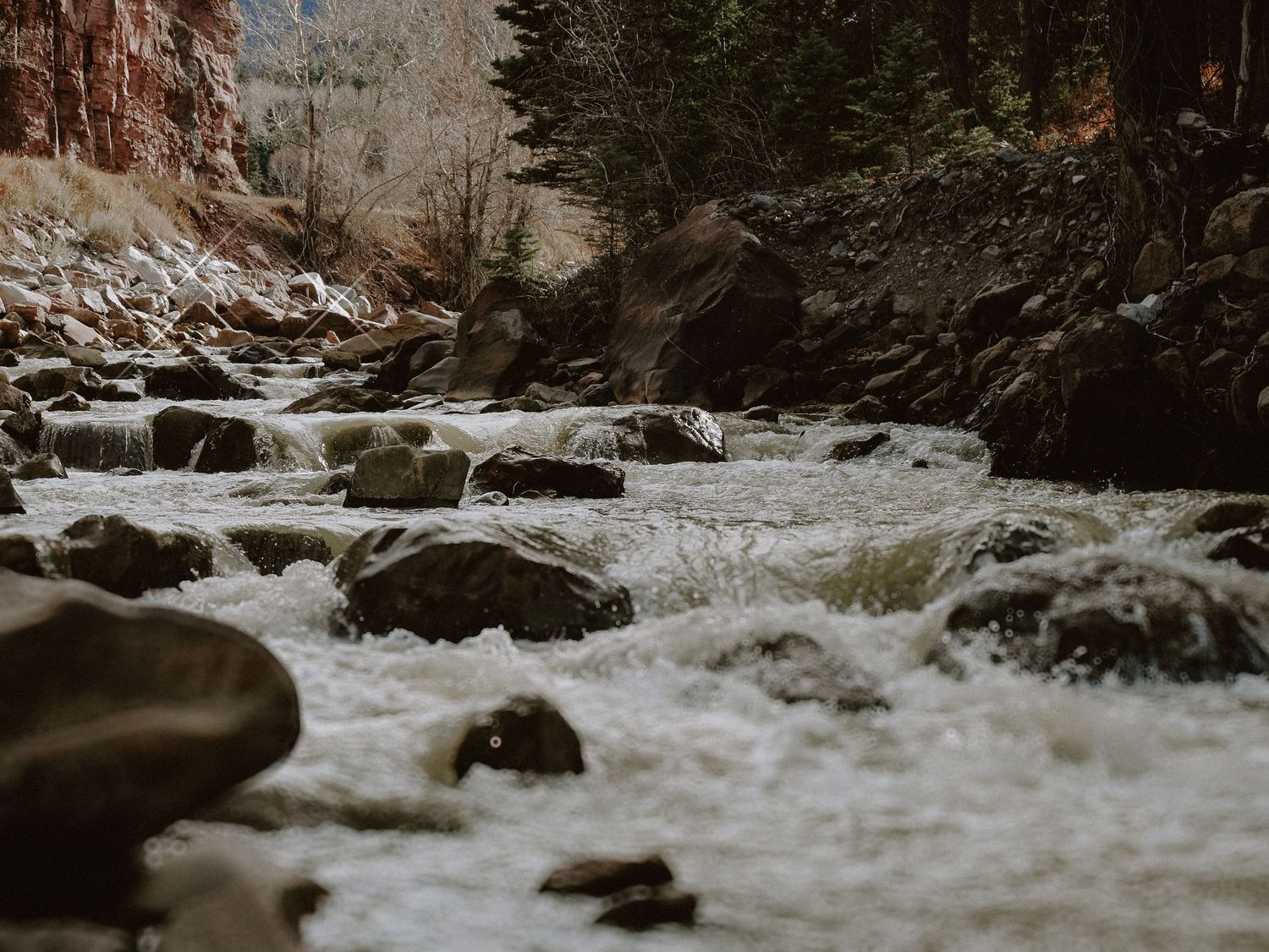 Cascading waterfalls flow over rocky terrain in a scenic winter landscape in Colorado.