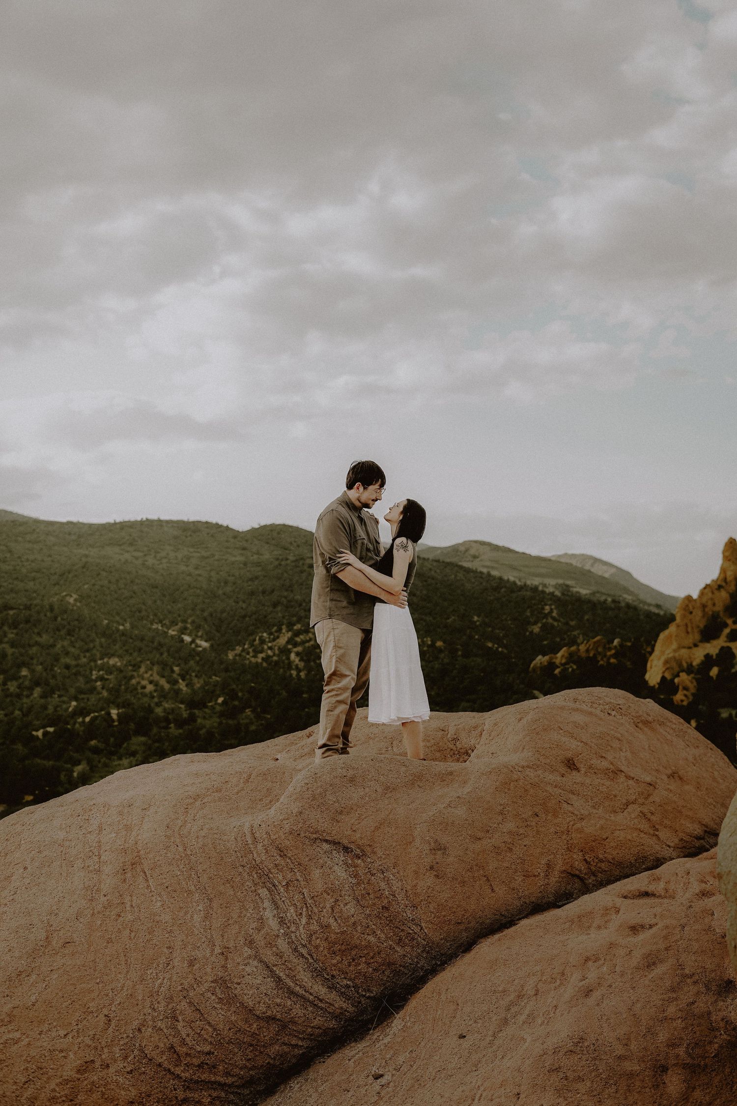 Silhouetted newly-engaged couple embraces on a rocky mountain overlook at Garden of the Gods during cloudy sunset.