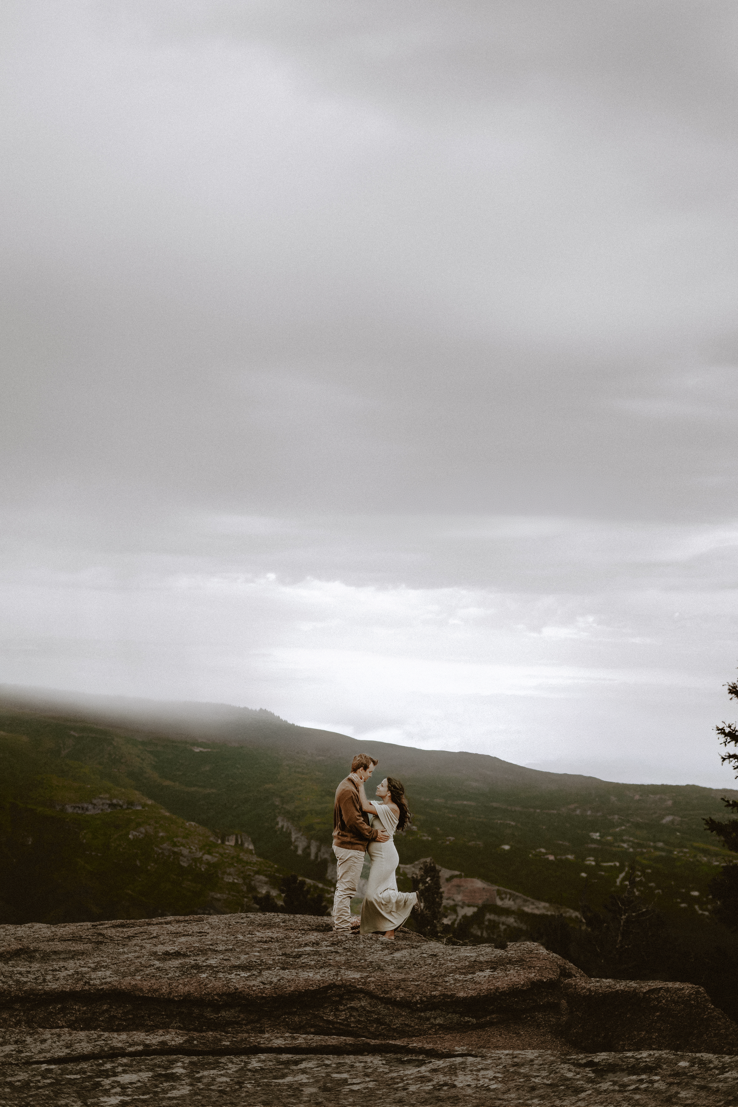 A couple on an adventure embraces on a rocky mountain overlook with dramatic cloudy skies in Manitou Springs, Colorado.