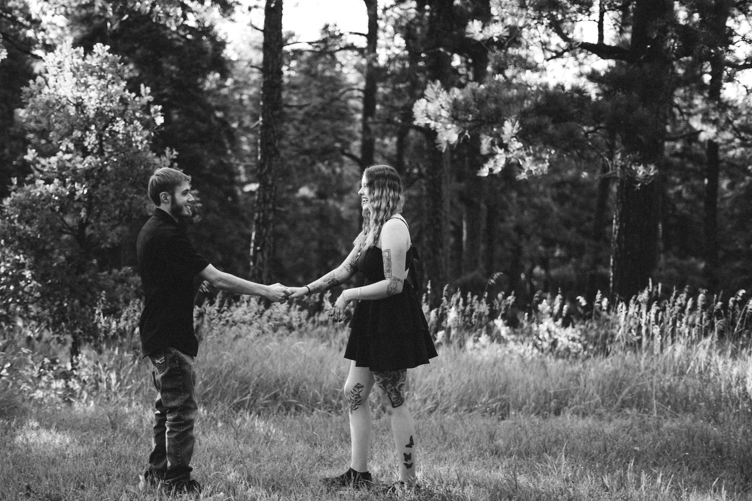 A couple dances playfully in a sun-dappled, adventurous meadow surrounded by tall pine trees around Pueblo Mountain Park.