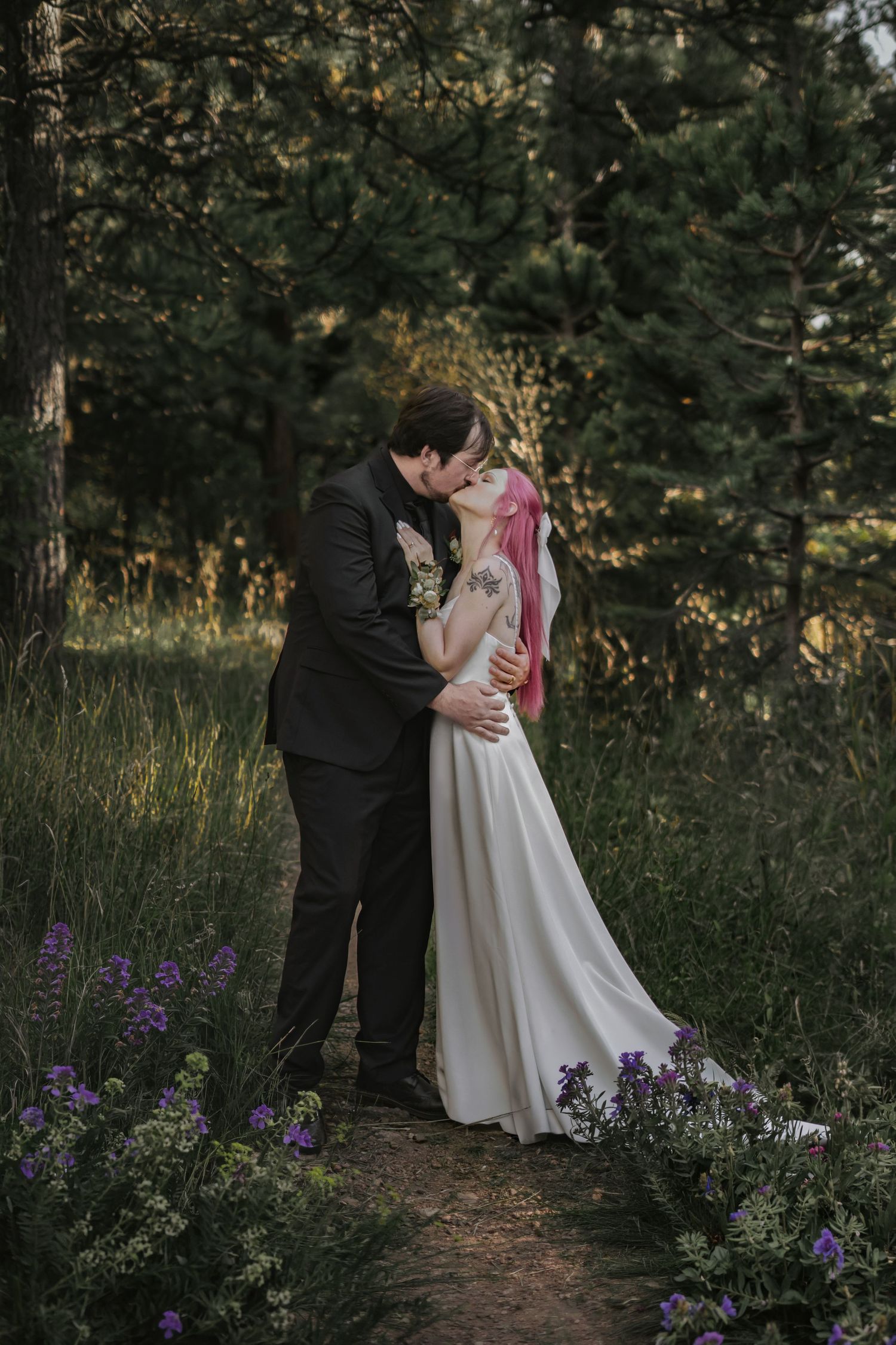 Elopement couple shares romantic moment among purple wildflowers on forest path in Pueblo Mountain Park.