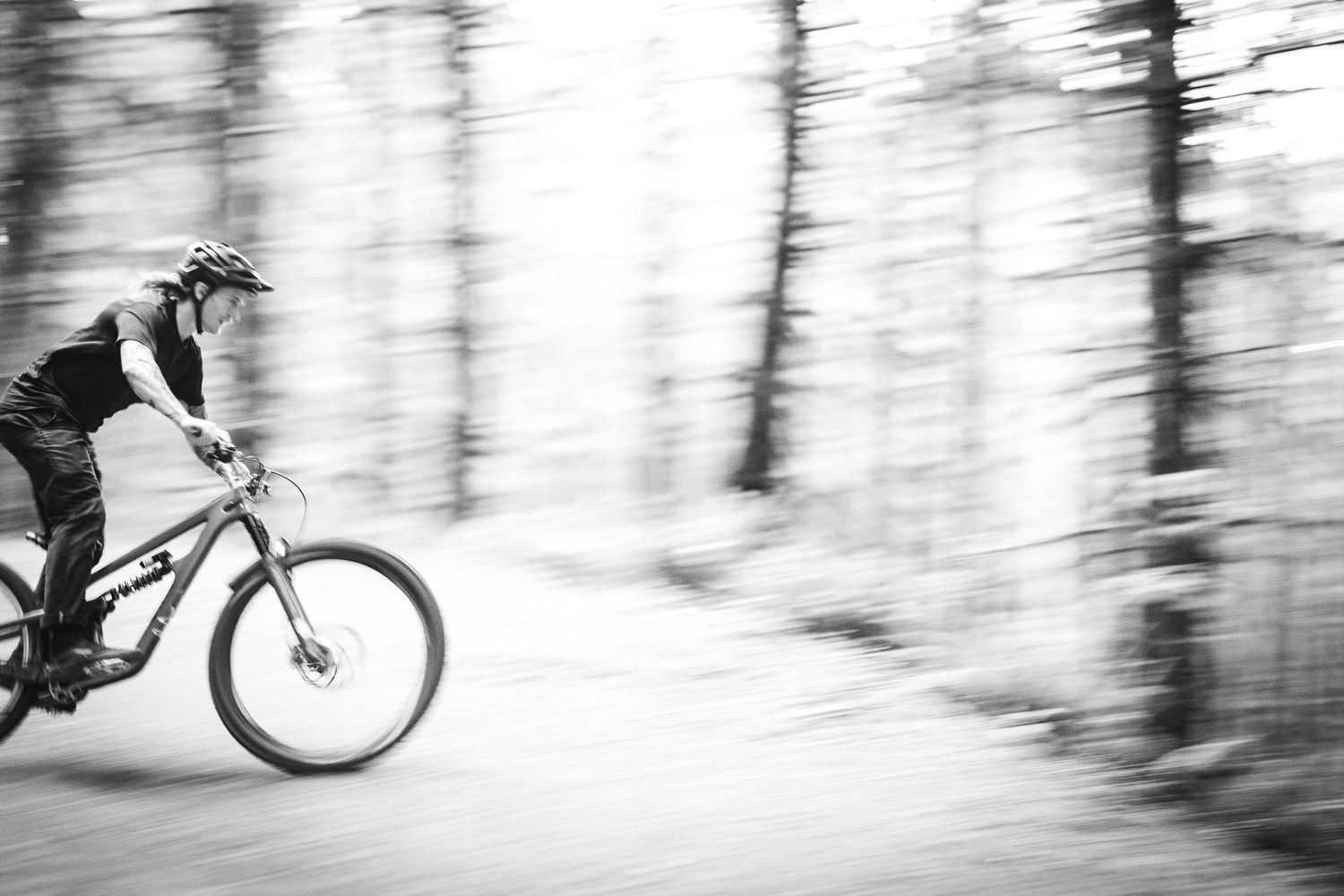 Black and white photo of a mountain biker speeding through a forest trail with motion blur effect.