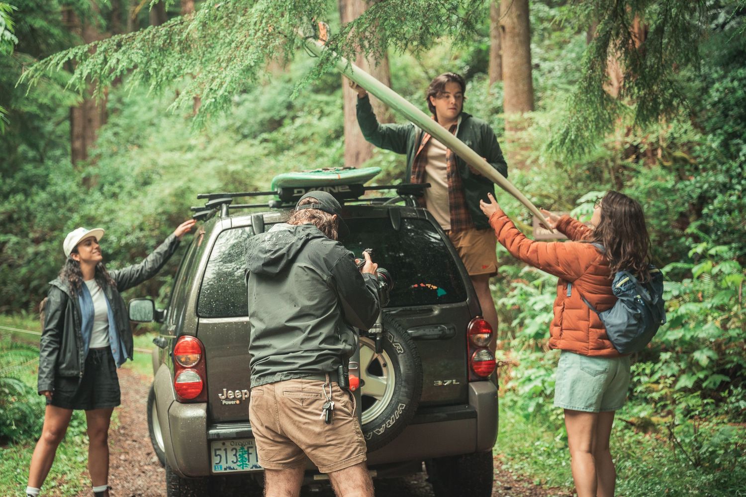 Group of hikers unloading gear from a Jeep in a lush green forest on an outdoor adventure trip.