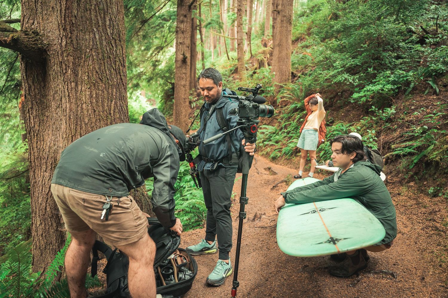 Film crew with camera equipment shooting on a forest trail among tall redwood trees outdoors.