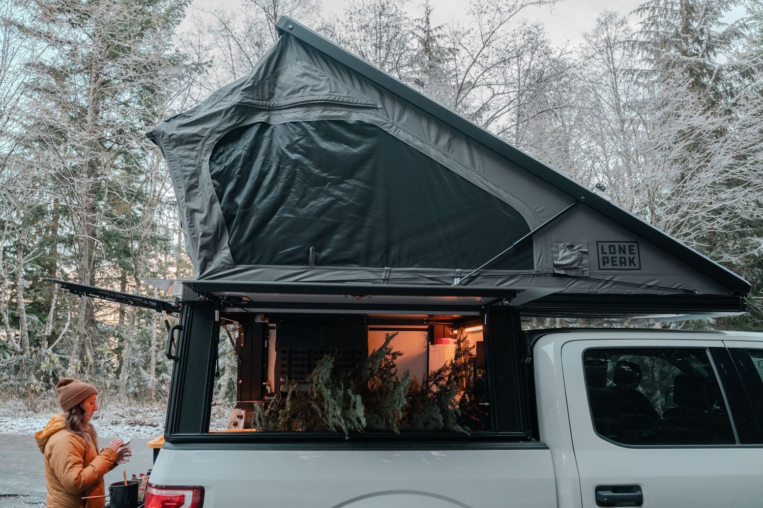 Black rooftop tent setup on a vehicle in a snowy winter forest setting.