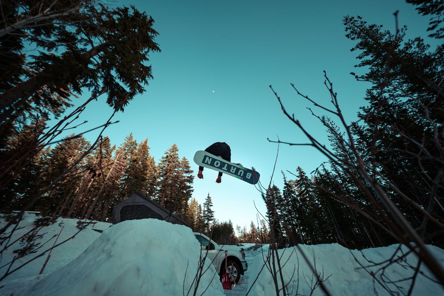 A scenic winter landscape with snow-covered evergreen trees silhouetted against a bright blue sky during sunset.