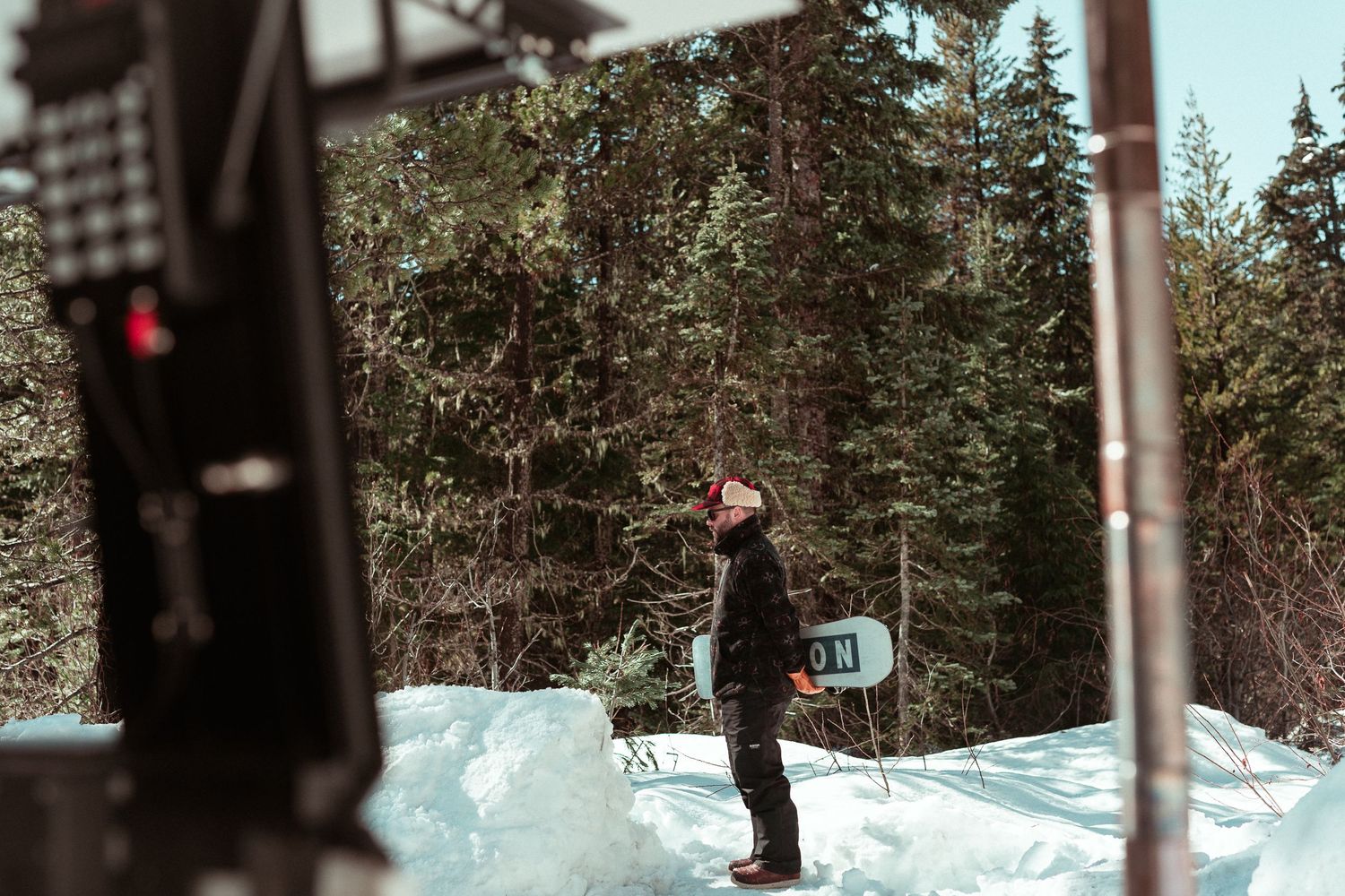 A person in winter gear stands in a snowy landscape surrounded by evergreen trees on a cold day.