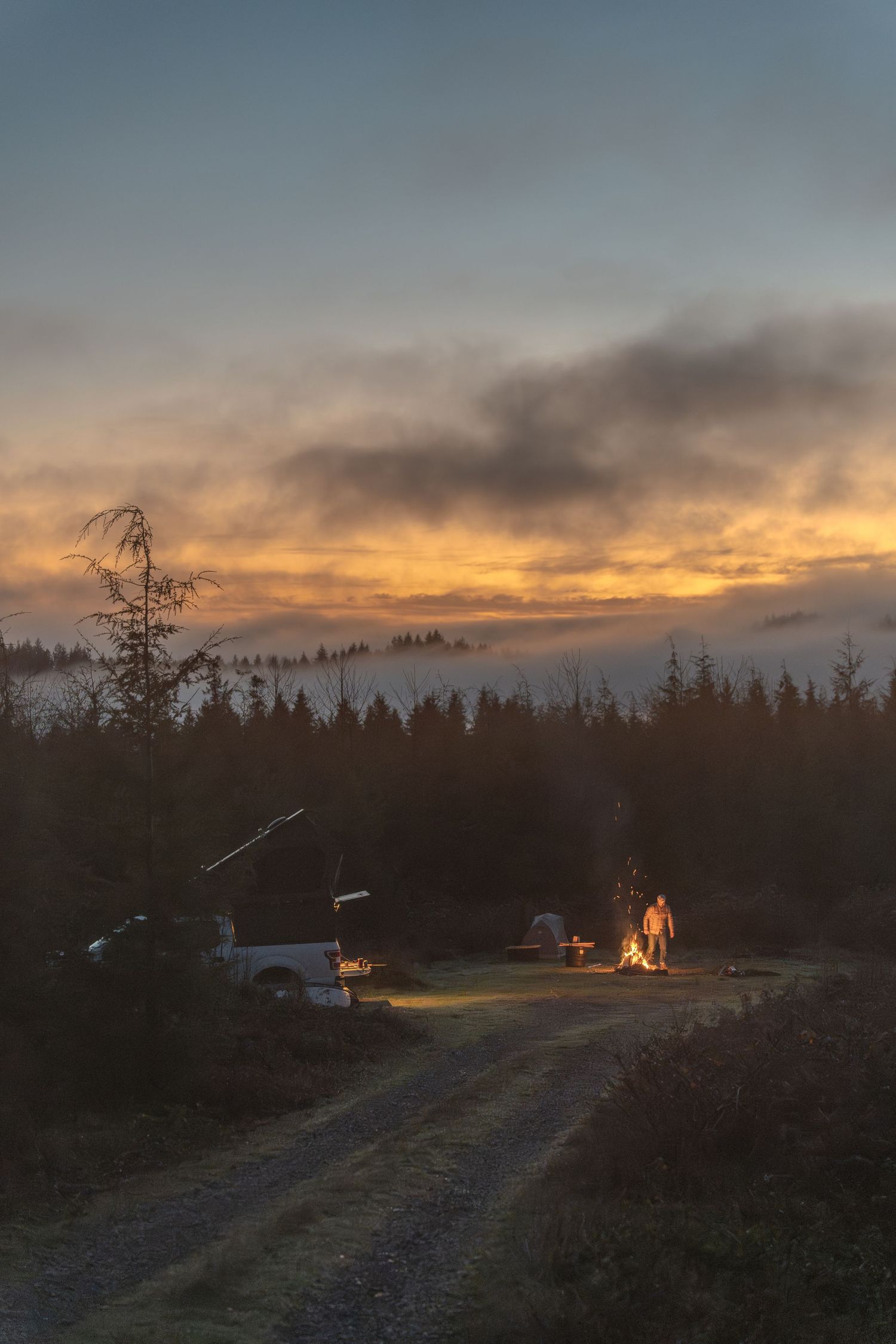 Dramatic sunset sky over a forest clearing with Lone Peak Camper silhouetted in the distance.