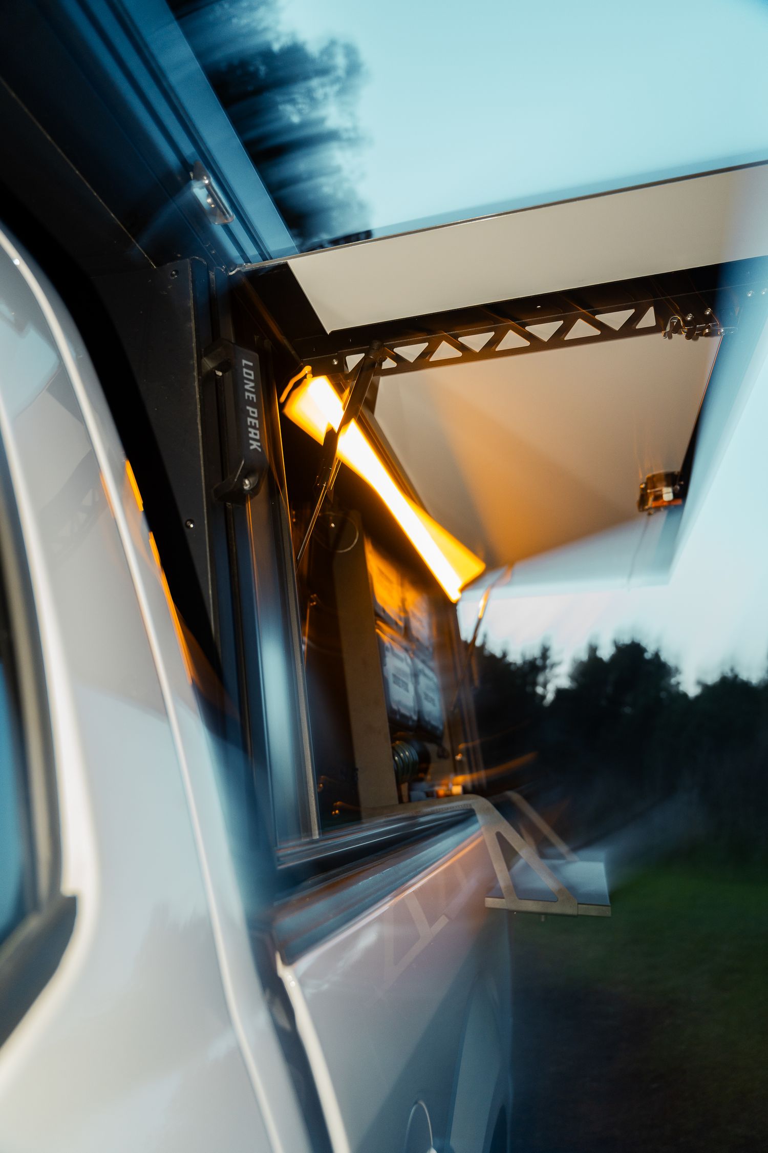 Interior vehicle view at dusk showing illuminated overhead lighting and structural supports.