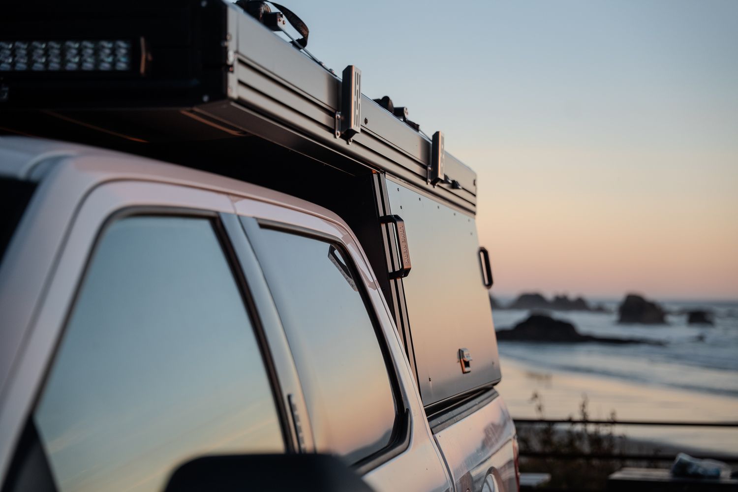 Close-up detail of a vehicle's roof rack and side window against a sunset coastal backdrop.