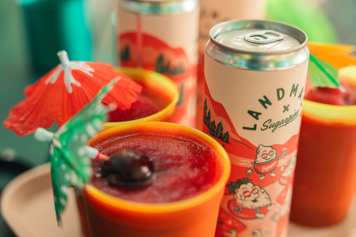 Landma x Sugarsnap canned drinks served in orange cups with red cocktails and decorative umbrellas.