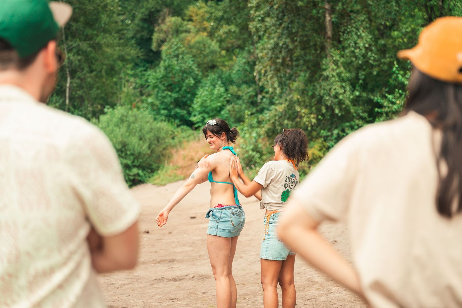 Group of young friends holding hands on a sandy path surrounded by lush green trees on a summer day.