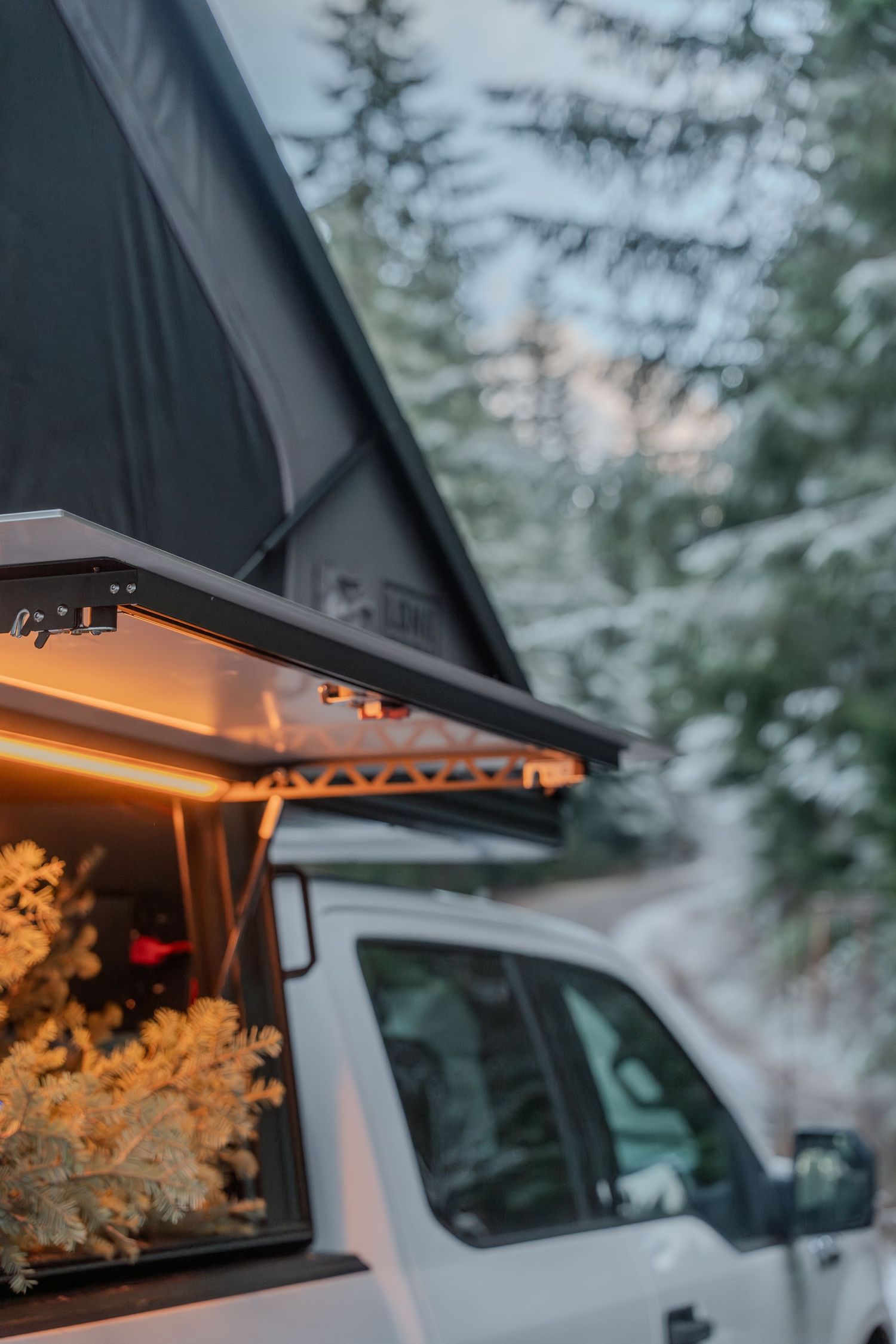 Close-up of a black rooftop tent with warm LED lighting and snow-covered trees in background.