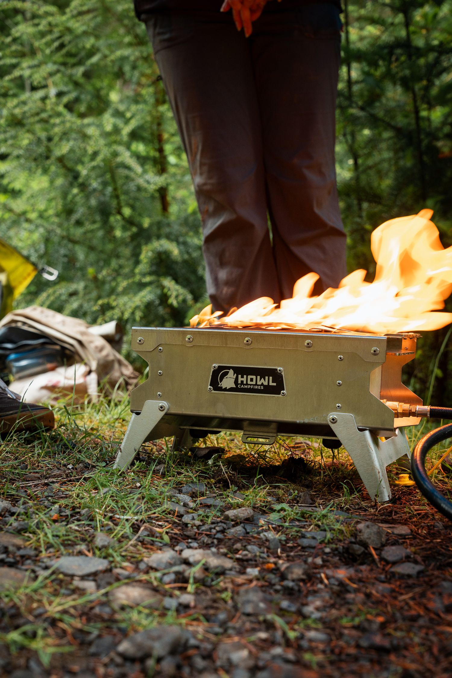 HOWL portable campfire pit with roaring flames in a forest campsite setting.