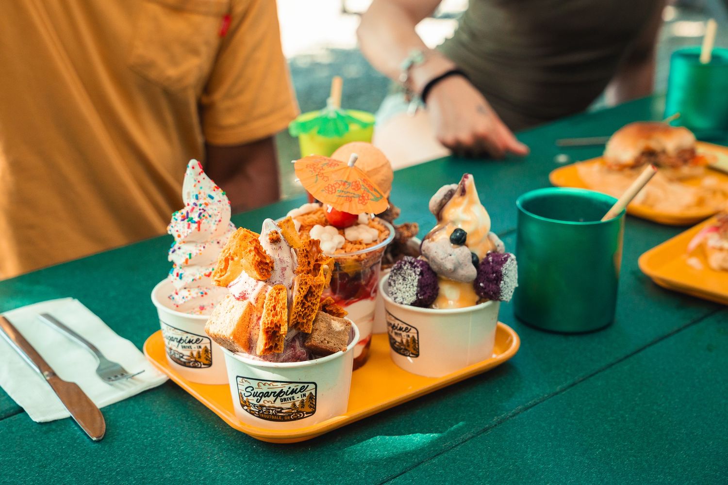 Colorful ice cream sundaes and desserts displayed on a yellow tray on a green tablecloth at an ice cream shop.
