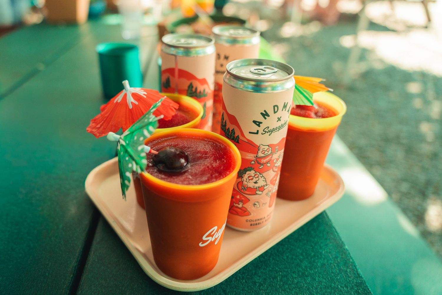Colorful orange cups with cocktails and canned drinks on a tray at an outdoor summer party gathering.