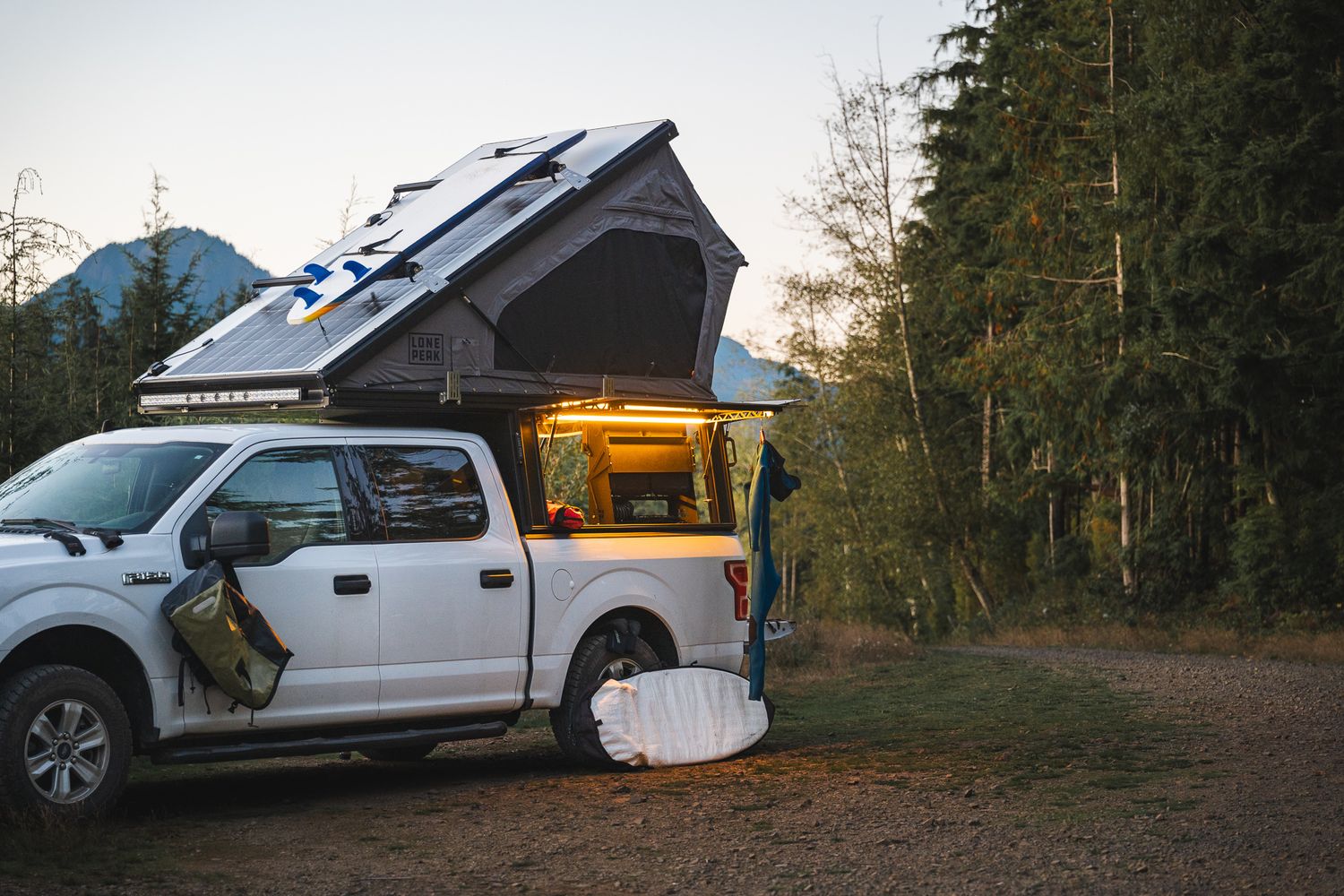 Panoramic view of multiple pickup trucks with rooftop tents parked in a forested camping area.