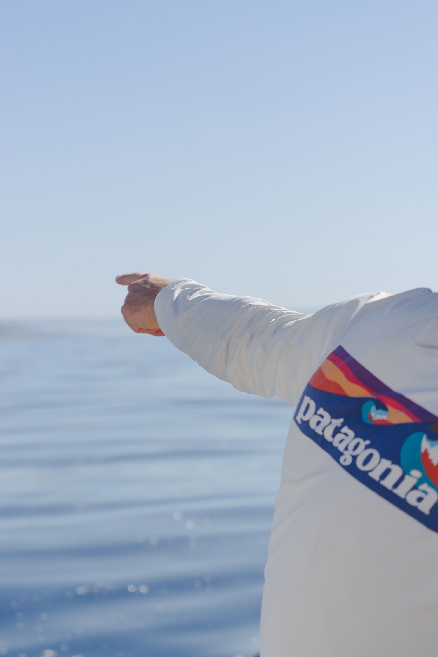 Person wearing a white Patagonia jacket pointing toward the ocean on a clear sunny day.